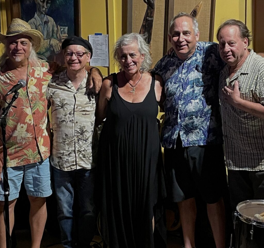 Five smiling adults posing indoors at music venue